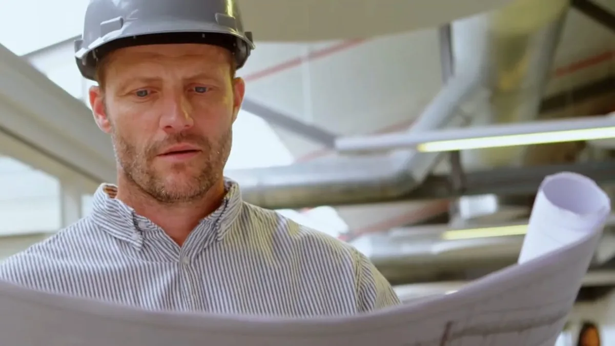 plumber reviewing drawings beneath overhead pipe runs shown in hero services 001 for Plumbing Services in Glendora, CA